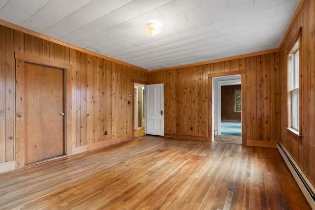 unfurnished bedroom with wooden walls, baseboard heating, and light hardwood / wood-style flooring