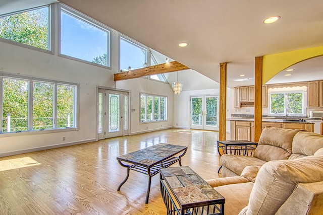 living room featuring sink, light hardwood / wood-style flooring, a chandelier, and high vaulted ceiling