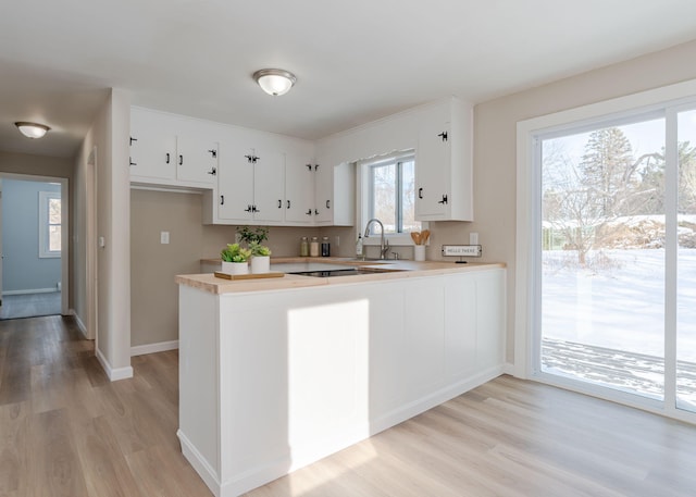 kitchen with kitchen peninsula, sink, white cabinetry, and light hardwood / wood-style floors