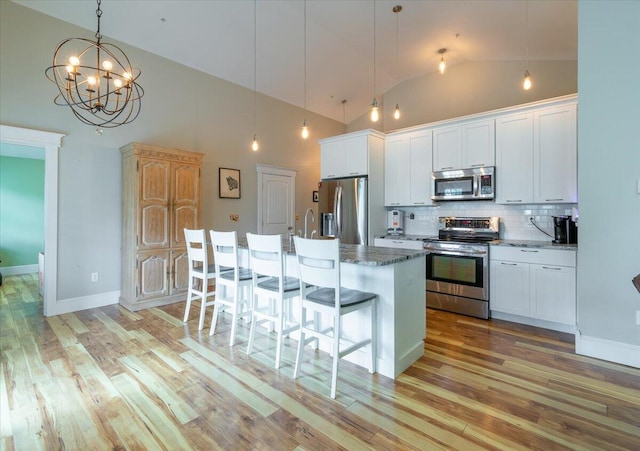 kitchen featuring white cabinets, a kitchen island with sink, appliances with stainless steel finishes, and hanging light fixtures