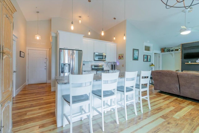 kitchen featuring light wood-type flooring, a breakfast bar area, white cabinets, high vaulted ceiling, and appliances with stainless steel finishes