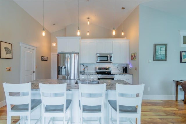 kitchen with pendant lighting, appliances with stainless steel finishes, white cabinets, and high vaulted ceiling