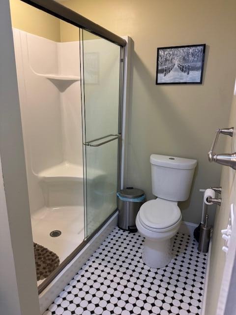 bathroom featuring tile patterned floors, a shower with shower door, and toilet