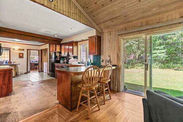 kitchen featuring a breakfast bar, kitchen peninsula, light parquet floors, lofted ceiling, and black fridge