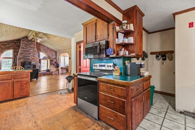 kitchen with light hardwood / wood-style floors, a brick fireplace, stainless steel appliances, vaulted ceiling with beams, and ceiling fan