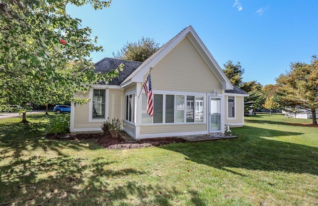 exterior space with a sunroom, roof with shingles, and a lawn