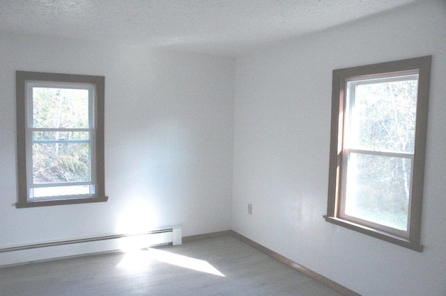 empty room with a textured ceiling, hardwood / wood-style floors, and a baseboard heating unit