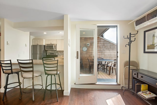 143 Beach Ave Unit 203, Kennebunk, ME 04043 - kitchen with appliances with stainless steel finishes, dark wood finished floors, a breakfast bar area, a wall unit AC, and light stone counters