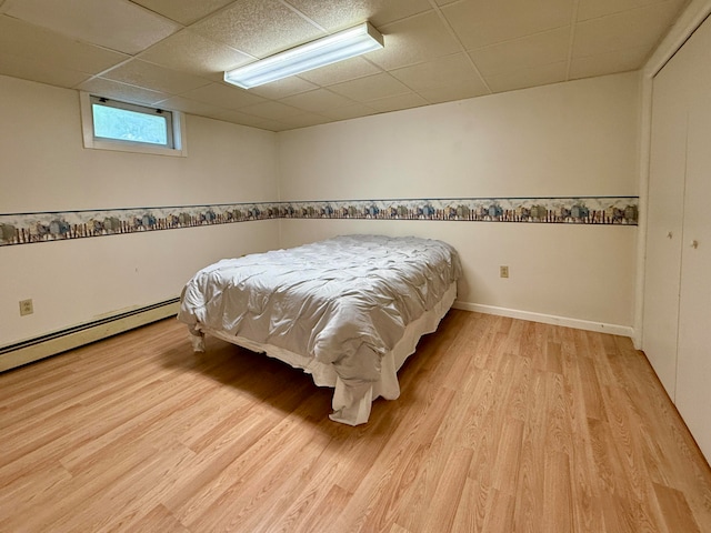 bedroom featuring a baseboard radiator, light hardwood / wood-style flooring, and a paneled ceiling