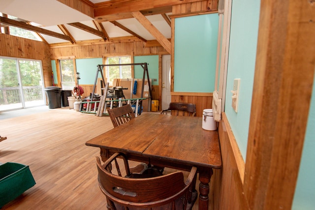 dining room with wood-type flooring, vaulted ceiling with beams, and wood walls