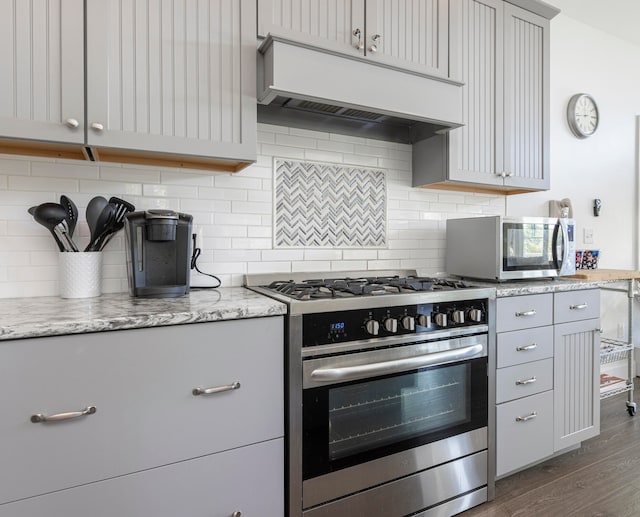 kitchen featuring gray cabinets, dark wood-type flooring, stainless steel appliances, light stone countertops, and backsplash