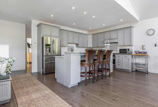 kitchen featuring a kitchen island with sink, gray cabinets, appliances with stainless steel finishes, a breakfast bar area, and dark hardwood / wood-style flooring