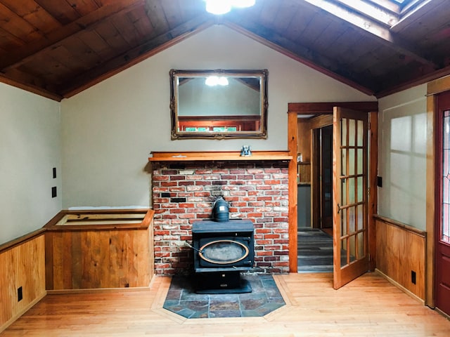 unfurnished living room with light wood-type flooring, a wood stove, lofted ceiling, wooden walls, and wooden ceiling