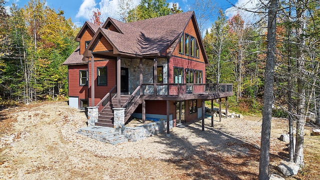 view of front of house featuring a shingled roof, dirt driveway, stone siding, stairs, and a deck