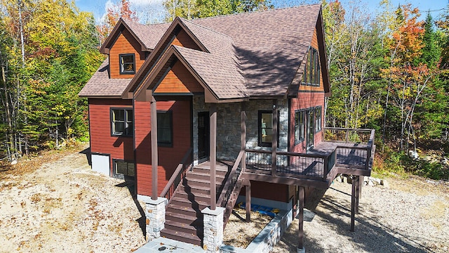 chalet / cabin with a shingled roof, stone siding, and a wooden deck