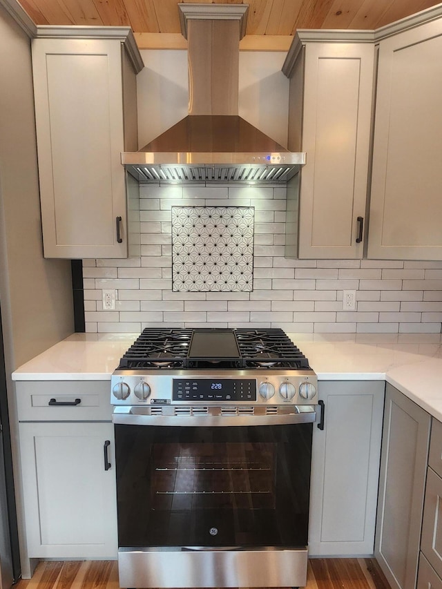 kitchen featuring light countertops, wall chimney range hood, gas stove, and gray cabinets