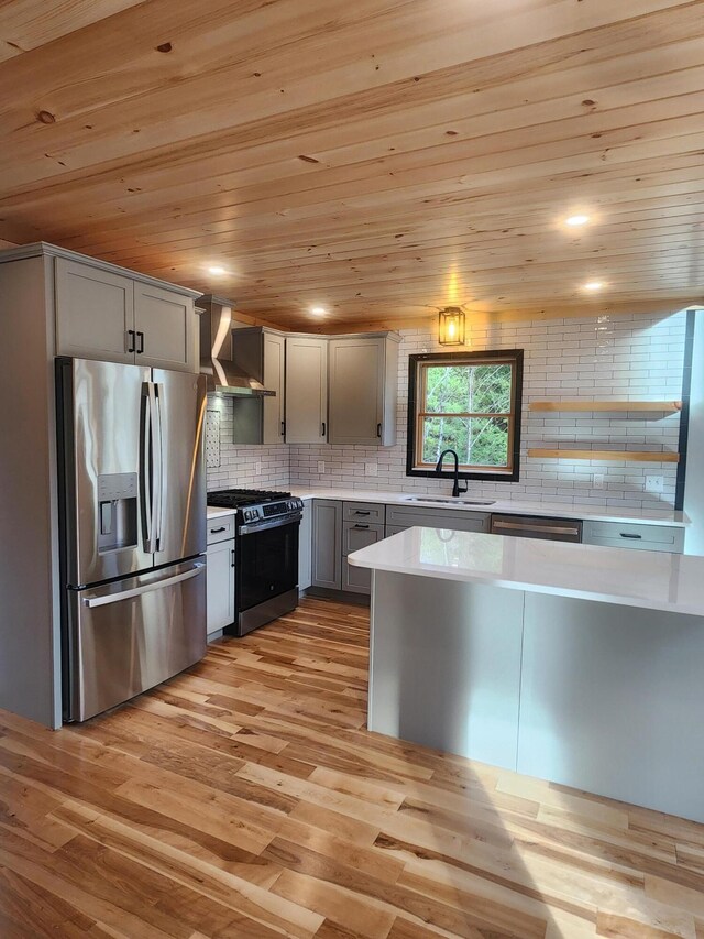 kitchen with appliances with stainless steel finishes, light wood-type flooring, wall chimney exhaust hood, sink, and gray cabinets