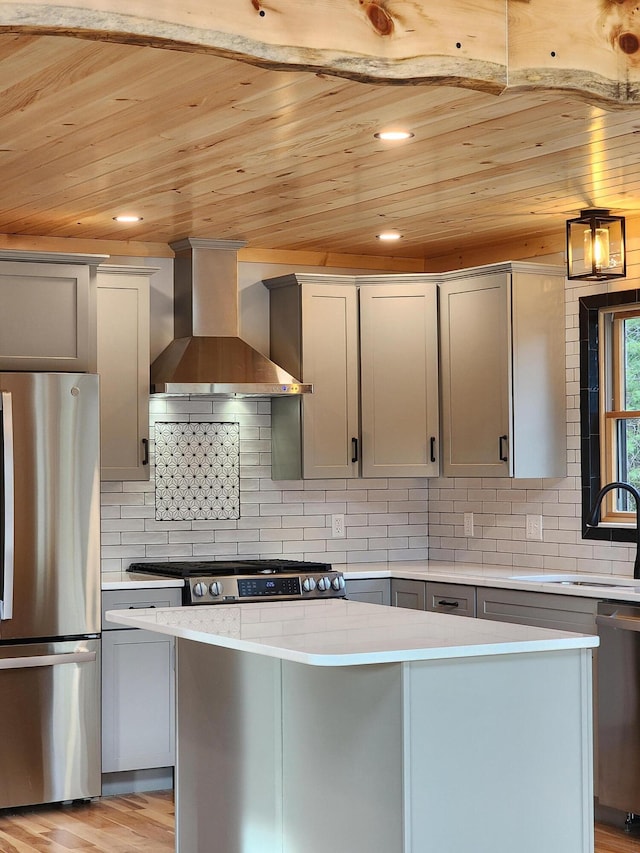 kitchen featuring a kitchen island, stainless steel appliances, light countertops, wall chimney range hood, and a sink