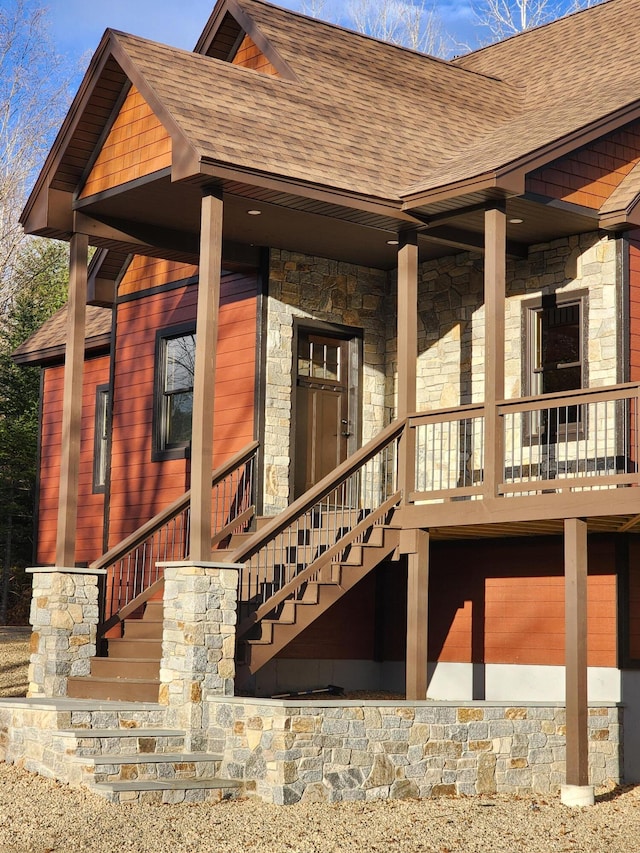 back of house with a garage, stone siding, stairs, and roof with shingles