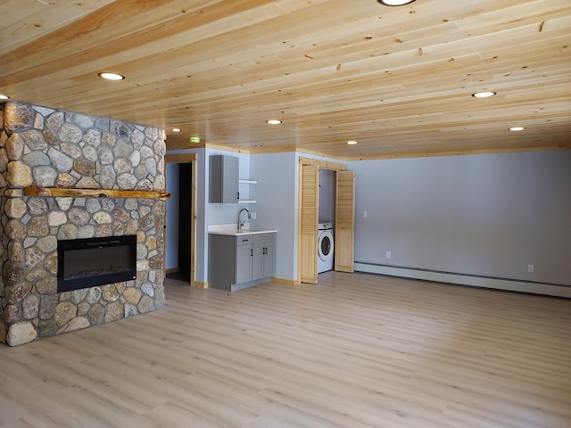 unfurnished living room with light wood finished floors, wooden ceiling, washer / clothes dryer, baseboard heating, and a sink