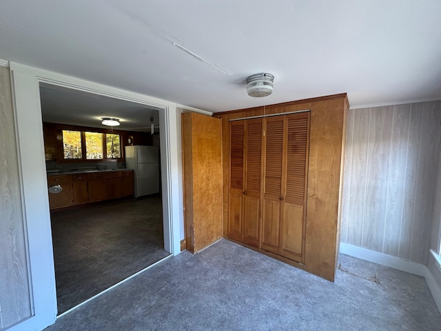 unfurnished bedroom with a closet, wooden walls, sink, and white refrigerator