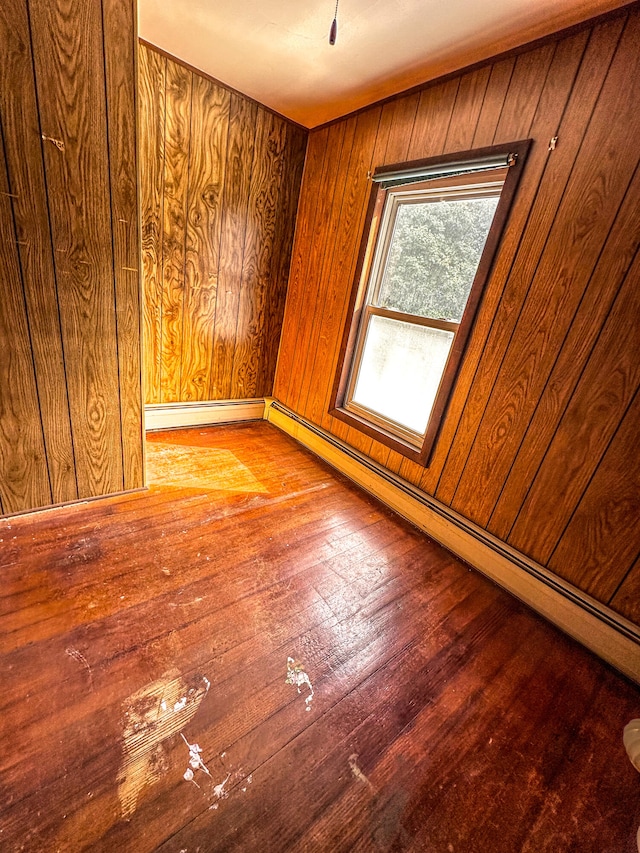 empty room with light wood-type flooring, baseboard heating, and wooden walls