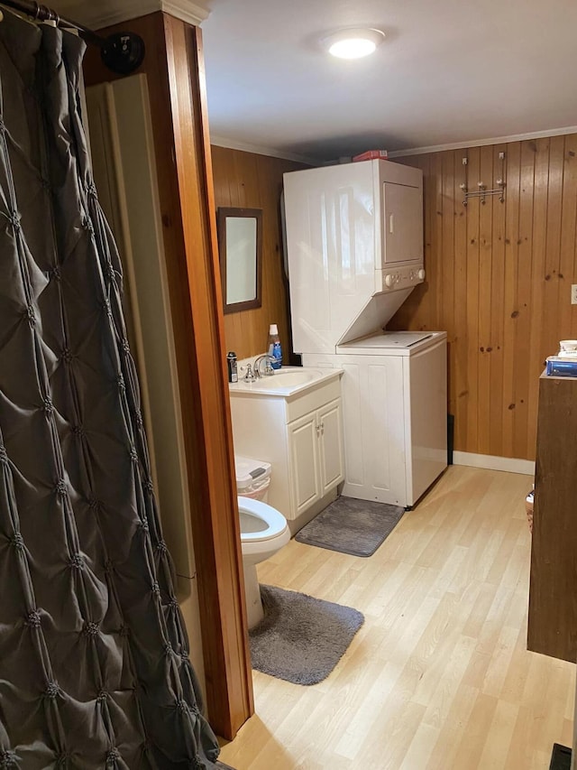 bathroom featuring vanity, wood-type flooring, stacked washer and clothes dryer, wooden walls, and toilet