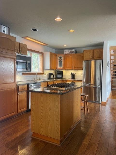 kitchen with decorative backsplash, a center island, appliances with stainless steel finishes, and dark hardwood / wood-style flooring