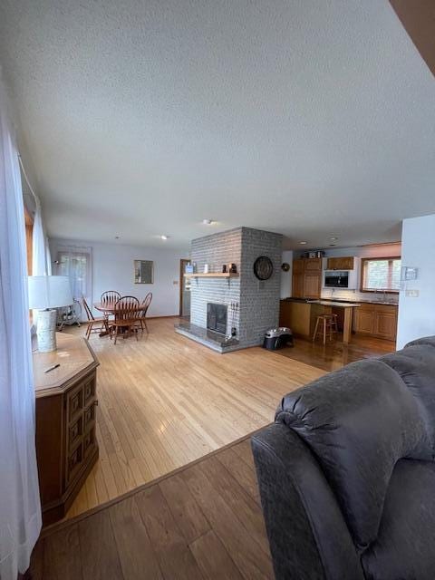 living room with a brick fireplace, a textured ceiling, and light hardwood / wood-style flooring