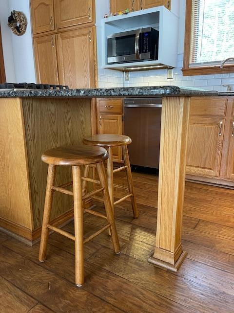 bar featuring appliances with stainless steel finishes, dark stone countertops, dark hardwood / wood-style flooring, and tasteful backsplash