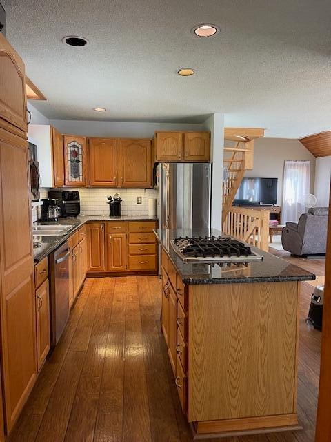 kitchen featuring light wood-type flooring, a textured ceiling, a center island, stainless steel appliances, and backsplash