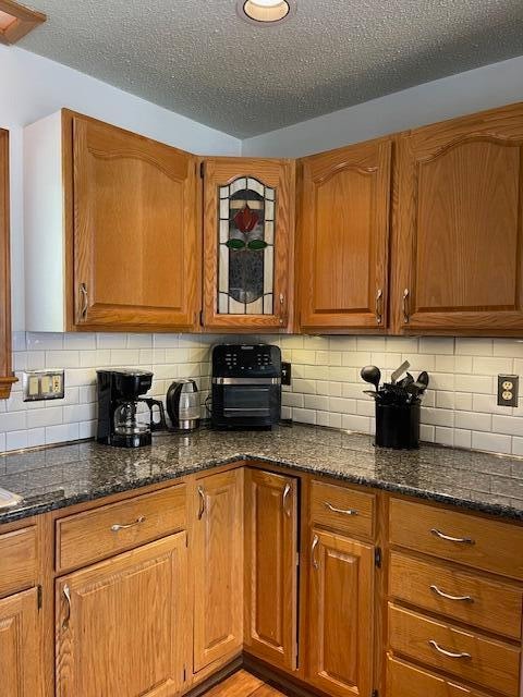 kitchen with decorative backsplash, dark stone countertops, light hardwood / wood-style floors, and a textured ceiling