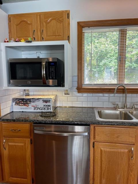 kitchen featuring decorative backsplash, stainless steel appliances, dark stone counters, and sink