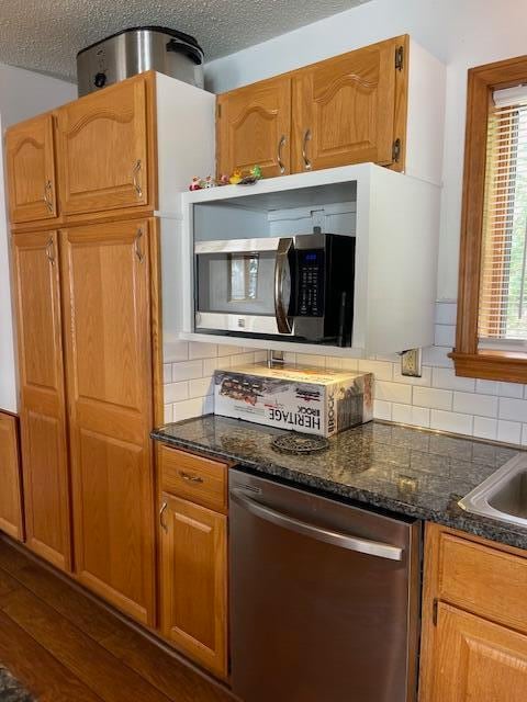 kitchen featuring decorative backsplash, dark wood-type flooring, stainless steel appliances, a textured ceiling, and dark stone counters