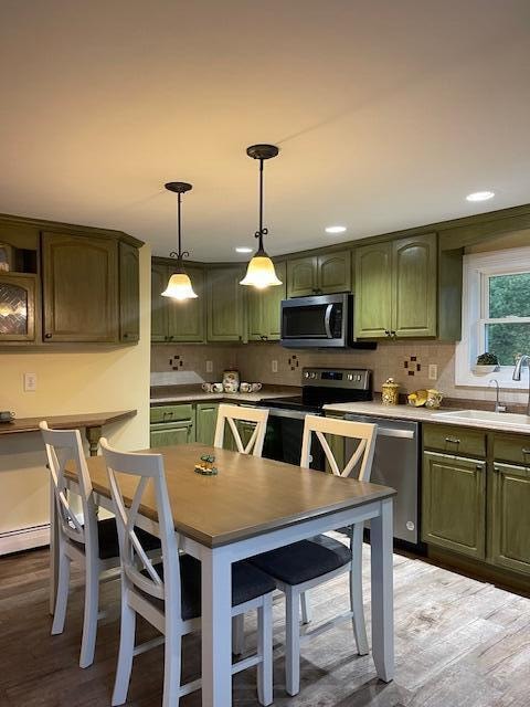 kitchen featuring hardwood / wood-style flooring, sink, hanging light fixtures, green cabinets, and appliances with stainless steel finishes