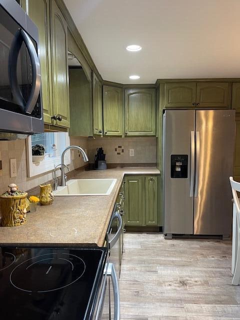 kitchen featuring sink, green cabinetry, backsplash, stainless steel appliances, and light hardwood / wood-style floors