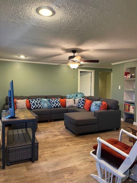 living room with ceiling fan, a textured ceiling, light wood-type flooring, and ornamental molding