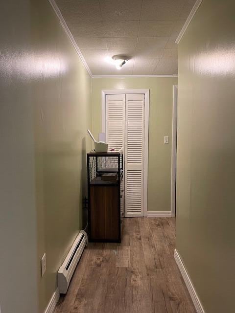 hall with a baseboard heating unit, hardwood / wood-style flooring, and crown molding