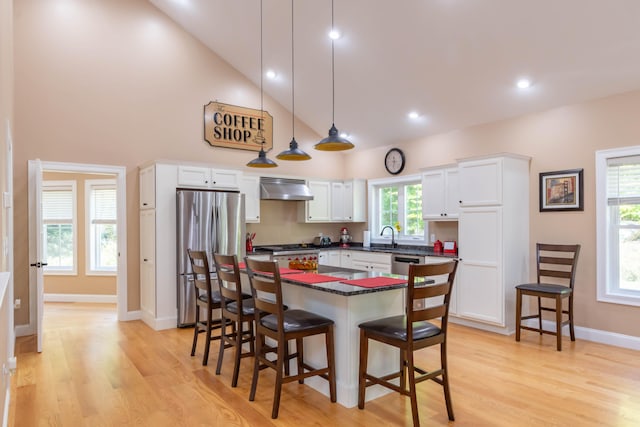 kitchen with high vaulted ceiling, white cabinets, stainless steel appliances, light hardwood / wood-style flooring, and decorative light fixtures