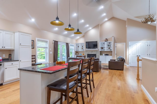 kitchen featuring white cabinets, decorative light fixtures, light hardwood / wood-style flooring, a breakfast bar, and dark stone counters