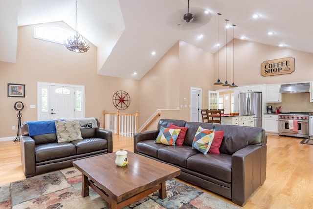 living room with ceiling fan with notable chandelier, light hardwood / wood-style flooring, and high vaulted ceiling