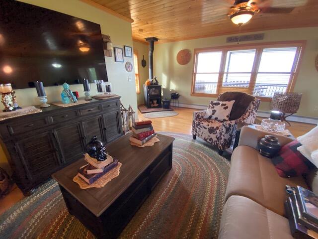 living room with wood-type flooring, ceiling fan, wooden ceiling, and a wood stove