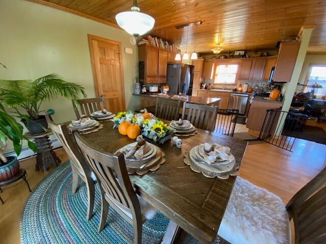 dining room with light hardwood / wood-style floors, wooden ceiling, and crown molding