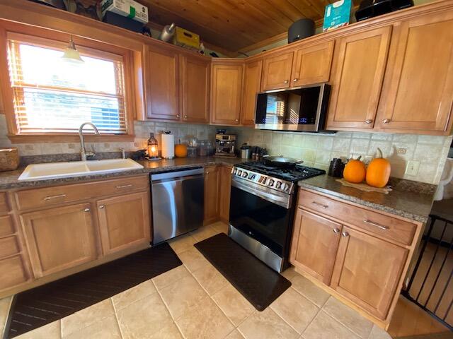 kitchen featuring dark stone countertops, wood ceiling, sink, stainless steel appliances, and light tile patterned floors