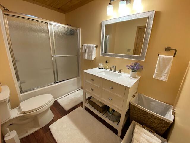 full bathroom featuring vanity, wood-type flooring, wood ceiling, bath / shower combo with glass door, and toilet