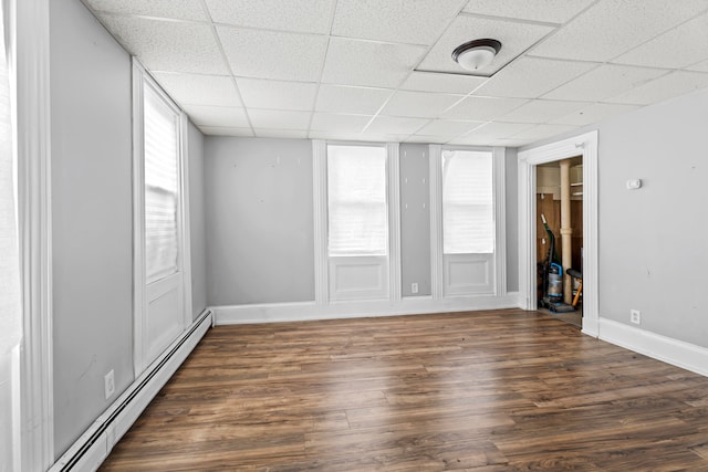 unfurnished room featuring baseboard heating, dark hardwood / wood-style floors, and a paneled ceiling