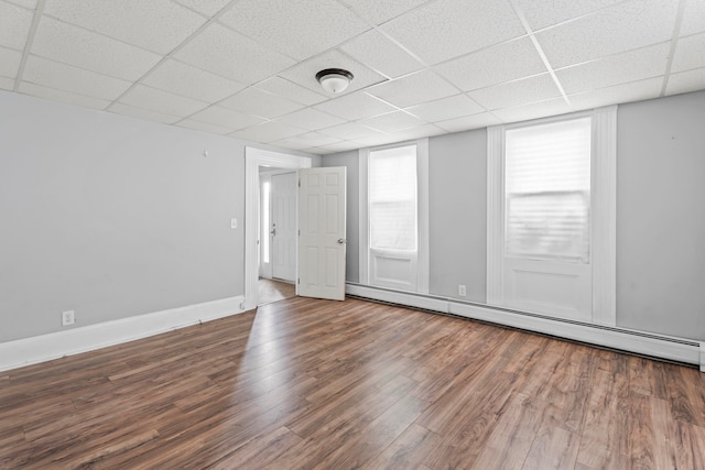 empty room with a drop ceiling, hardwood / wood-style floors, and a baseboard heating unit