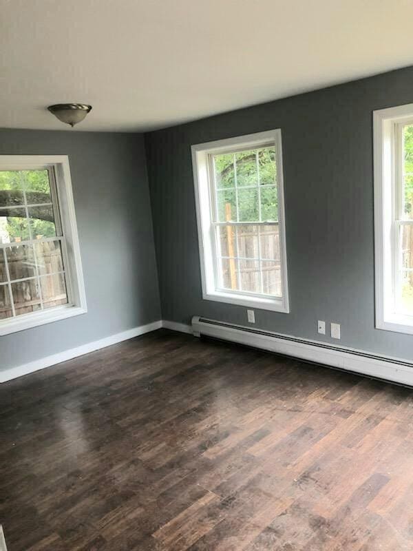 empty room with dark wood-type flooring and a baseboard heating unit