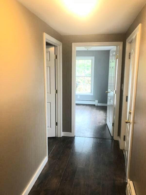 corridor featuring baseboard heating and dark wood-type flooring