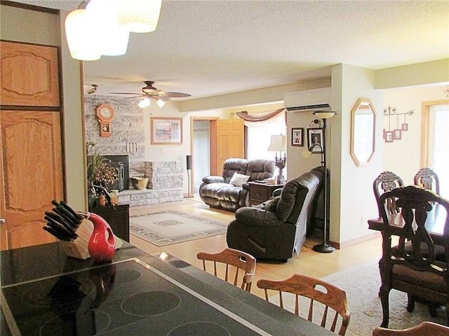living room featuring a textured ceiling, a stone fireplace, a ceiling fan, and a wall mounted air conditioner
